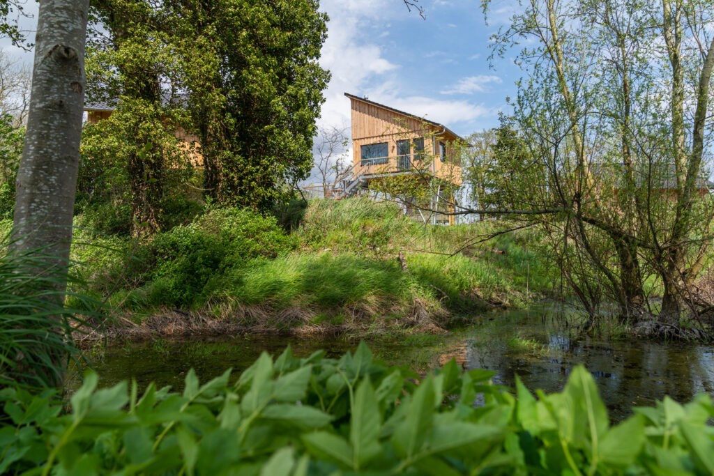 Stelzenhaus im Baumhaushotel Otterndorf zwischen Bäumen, Naturteich im Vordergrund